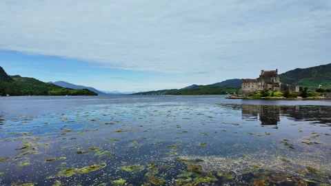 Pan from a green mountain range at Loch Duich to the historic Eilean Donan Stock Footage 342214801