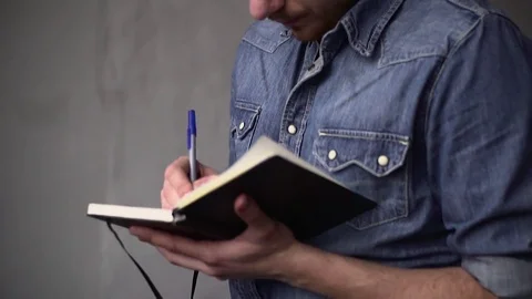 PAN of the guy writes in the notebook while standing near the window opposite Video stock 82904703