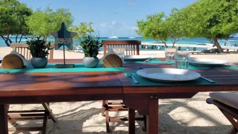 Pan left over dining table set on Caribbean beach, with birds, docks, turquoise Vídeo Stock 313649860