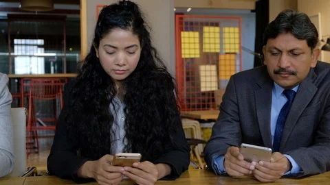Pan left to right and back on four Indian colleagues busy transfixed on their sm Stock Footage 101890046