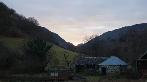 Pan from left to right with mountains and tree to a sunset above a farmhouse Stock Footage 101759493