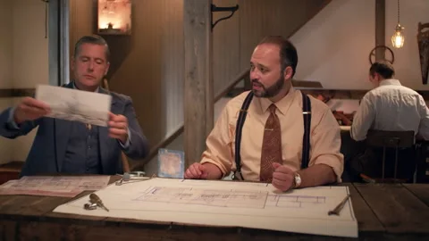 Pan-left shot of two businessmen reviewing blueprints, 1950s, USA - Reenactment Stock Footage 245290559