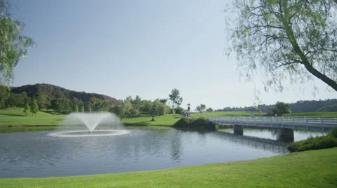 Pan left wide view of a golf course with a fountain, lake, and bridge. Vidéo 34481148