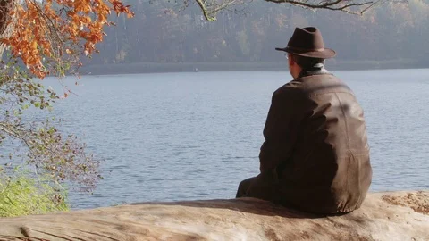 Pan to a Lonely Man, he is Sitting above a Lake an looking to a Boat. Видео 76205652