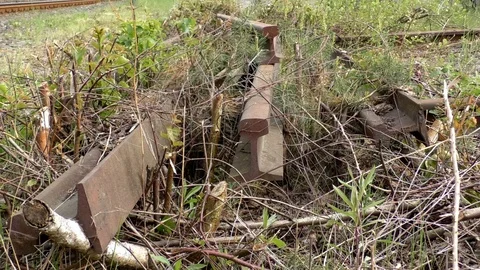 Pan: Old steel stracks lying next to a railway, plants growing over the tracks Stock Footage 89306586