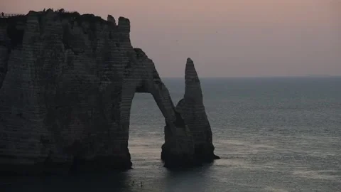 Pan over the Porte d'Aval arch and Aiguille silhouetted against a pink dusk sky Stock Footage 344532252