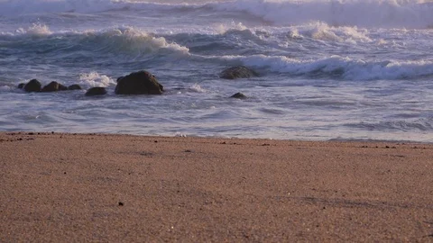 Pan up over sandy beach to rough, white, choppy surf waves on the stormy sea. Video stock 105157369
