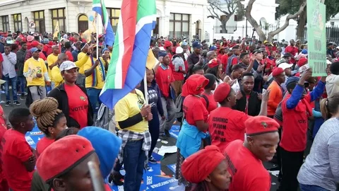 Pan overhead view of singing &amp; dancing people with flags &amp; placards wearing red  Vidéo 78617135