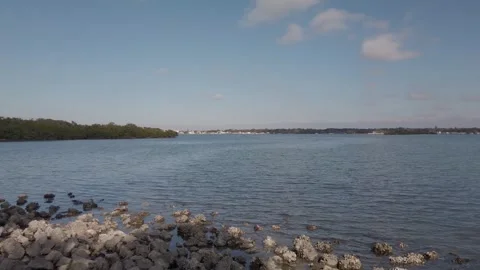 Pan, pan view, View over rocks towards blue bay water with blue and white clouds Stock Footage 260636533