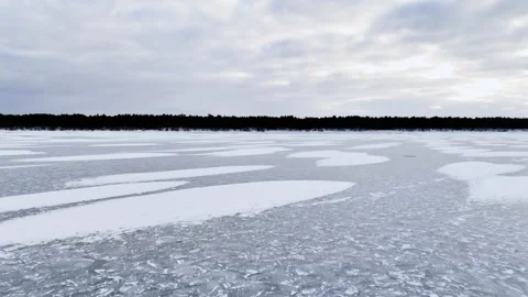 Pan up from patterned frozen ice to cloudy winter sky over a flat shoreline Stock Footage 333033007