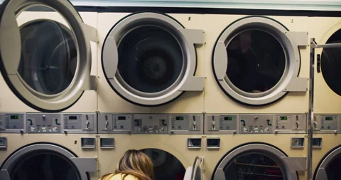 Pan of people doing laundry in interior small laundromat with bright interior li Stock Footage 199461414