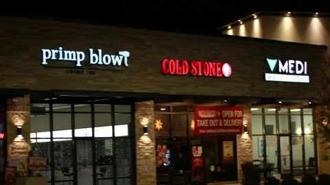 Pan of Primp Blow Cold Stone and retail oulets at night Stock Footage 143810464