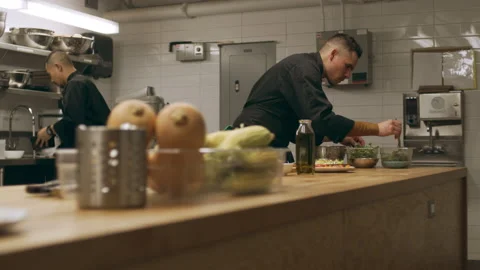 Pan of professional chefs working at their stations at a long counter in industr Stock Footage 199457475
