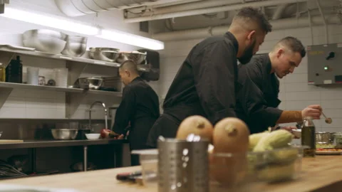 Pan of professional chefs working at their stations at a long counter in industr Stock Footage 199457847