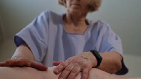 Pan Up Rack Focus from Senior Back and Masseur Hand to Therapist’s Face Video stock 311423489