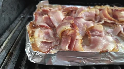 Pan from right across cooked bacon rashers on aluminum foil, viewed from above. 스톡 동영상 334642240