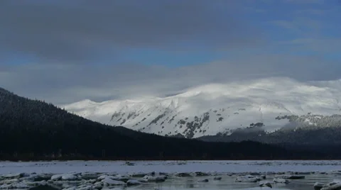 Pan Right Snow Covered Mountains with Icy River in Foreground Stock Footage 38056153