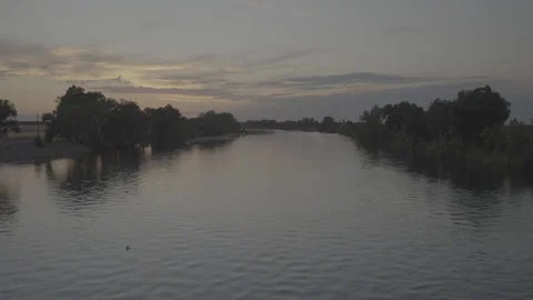 Pan up to a river during sunset with plane flying over Stockbeeldmateriaal 251896558