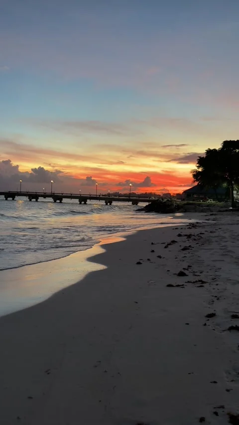 Pan round beach at sunset towards Oistins Pier, Barbados in the Caribbean. Stock Footage 333280916