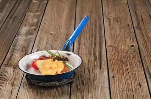 Pan with scrambled eggs and herbs on wooden table Stock Photos