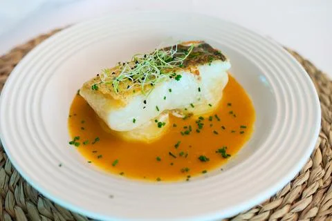 Pan seared white fish serving with orange sauce and sprouts Fotos de archivo