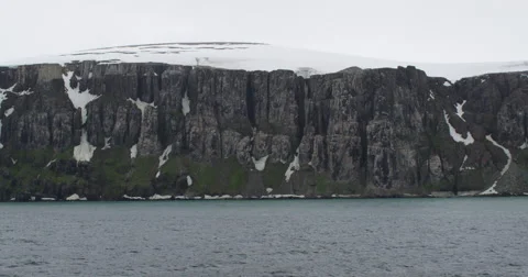 Pan of seaside bird nesting cliffs with snow and clouds Stock Footage 56626534