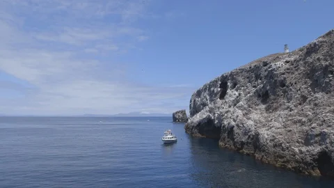 Pan of Ship Sitting Next to Coastline Rock Wall Lighthouse Anacapa Island Stock Footage 121526643