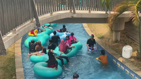 Pan shot of a bridge and pool at the bottom with people enjoying the pool Stock Footage 255694890