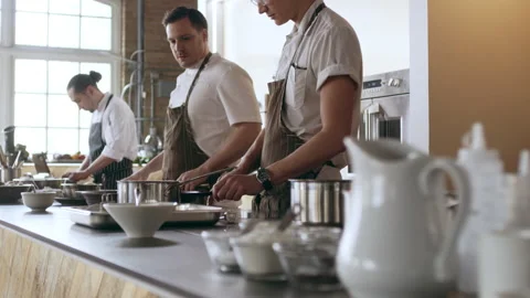 Pan shot of focused professional chefs cooking on a large counter top full of po Stock Footage 199457009