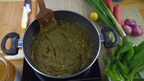 Pan shot of hands cooking Sarson ka saag on induction cooker - Punjabi cuisine Stock Footage 128692638