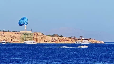Pan shot of parasailing over the Red Sea with speedboat and yachts near a rocky Video stock 331494412