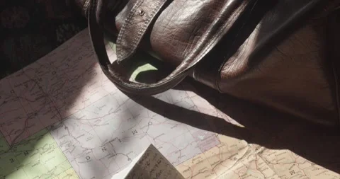 Pan shot reveals handwritten mail on a road map beside a leather bag, creating Stock Footage 344348080