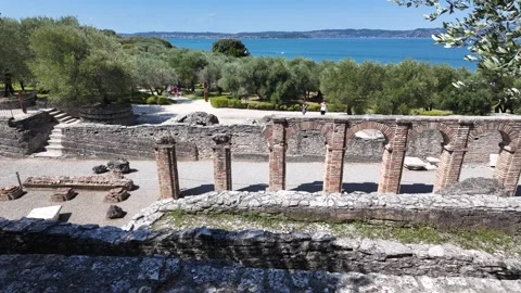 Pan shot of Roman columns and arches with olive trees and lake Garda on distance Stock Footage 342394893