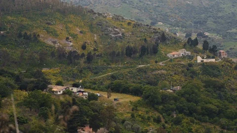 Pan from small houses in the middle of trees to a small town between hills Stock Footage 88686210
