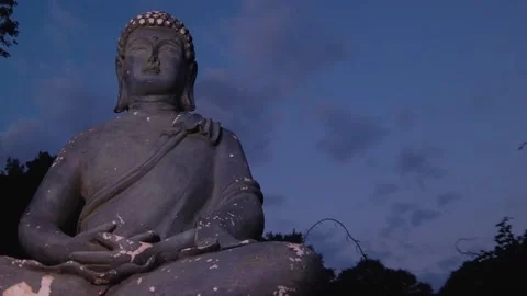 Pan up a statue of the Buddha with time lapse of evening sky turning dark Stock Footage 137719396