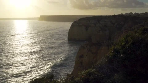 Pan to sunset over ocean with cliffs and reflection Stock Footage 273674617