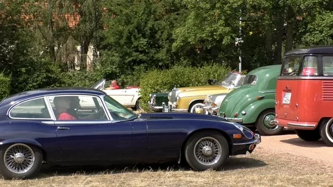 Pan: Two elderly men driving historic dark blue Jaguar E-Type at oldtimer event Stock Footage 114440225