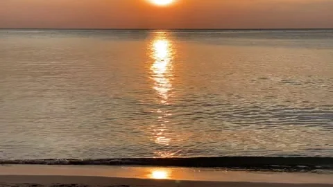 Pan up from water lapping at sandy beach to beautiful sunset over the water Video stock 233272595