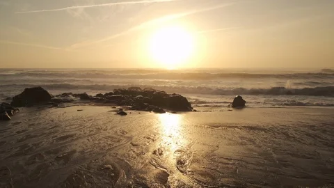 Pan up from wet sand on beach at sunset, to ocean with sunlight reflected Stock Footage 116756477