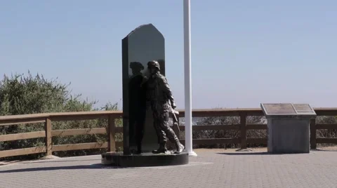 Pan up from World War II bronze statue below american flag in strong wind on Stock Footage 67556160