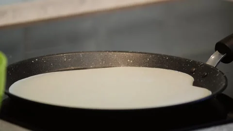 Pancake batter sizzling on an induction stove transforms into a delicate crepe Stock Footage 296847441