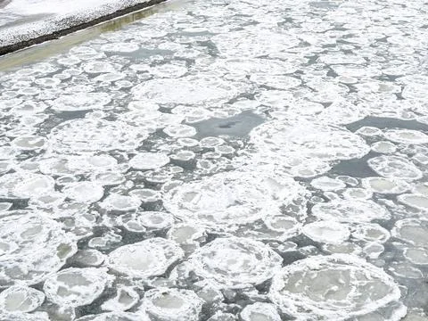 Pancake ice chunks float on the dark freezing surface of a river during deep Stock Photos