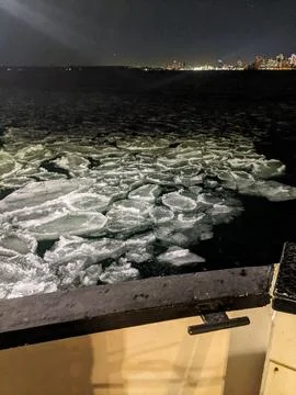 Pancake Ice Floating in Dark Winter Water at Night with City Skyline Фото