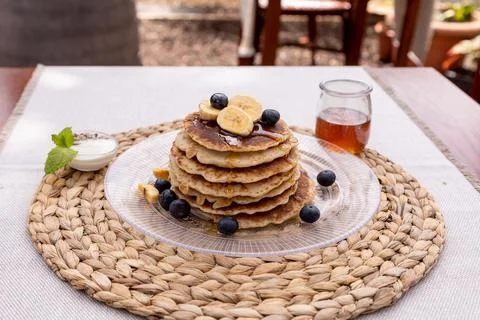 Pancake stack with syrup, bananas and blueberries on a glass plate with a handma Stock Photos