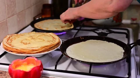 Pancakes are thin in the process of frying in two frying pans on a gas stove Stock Footage 149403240