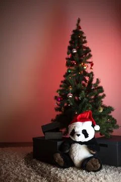 Panda plush in Santa hat under Christmas tree in soft red glow Stock Photos