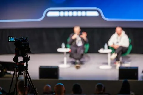 Panel discussion on stage with two speakers and camera recording audience at 库存照片