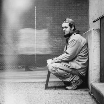 Panhandler sits while blurred pedestrians pass him by Stock Photos