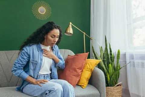 Panic attack. A young Latin American woman is sitting at home, holding her chest Foto stock