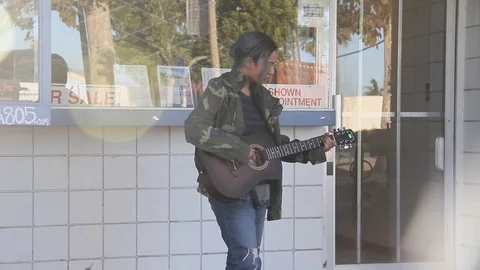 Panning from the bright light to kid on guitar in front of shop Stock Footage 122724457